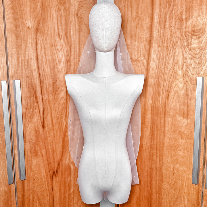 A front view of a fingertip length wedding veil featuring scattered rhinestones and pearls draped over a bridal silhouette.