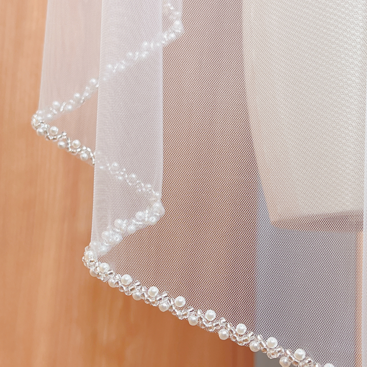 Fingertip length beaded edge wedding veil crafted from sheer soft tulle fabric.