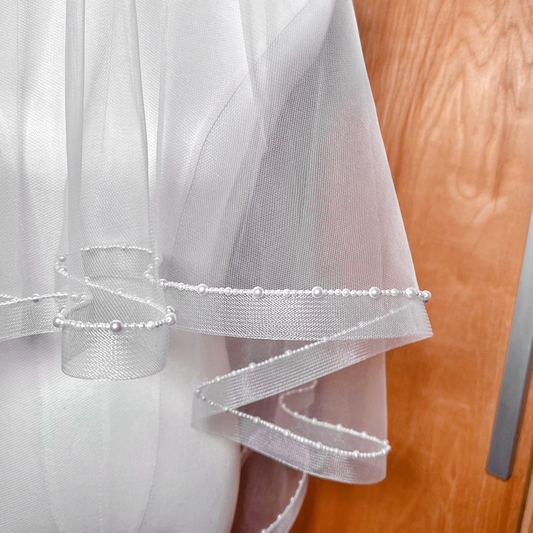 Close-up of the delicate pearl trim and horsehair edging on a fingertip length two-tier veil.