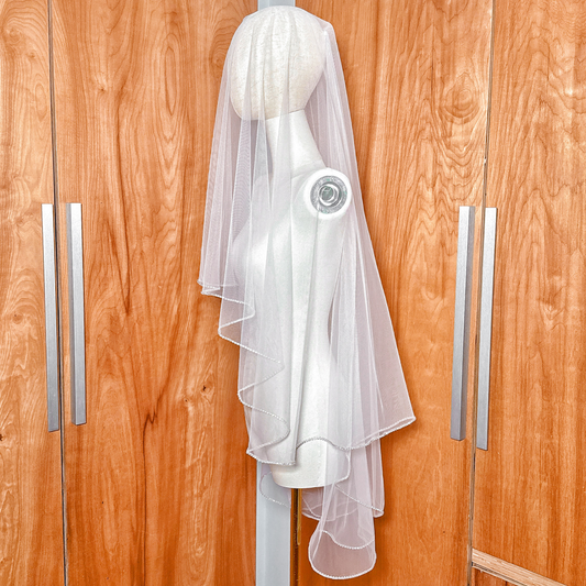 Two tier wedding veil with rhinestone edge cut to fingertip length on a white display torso.