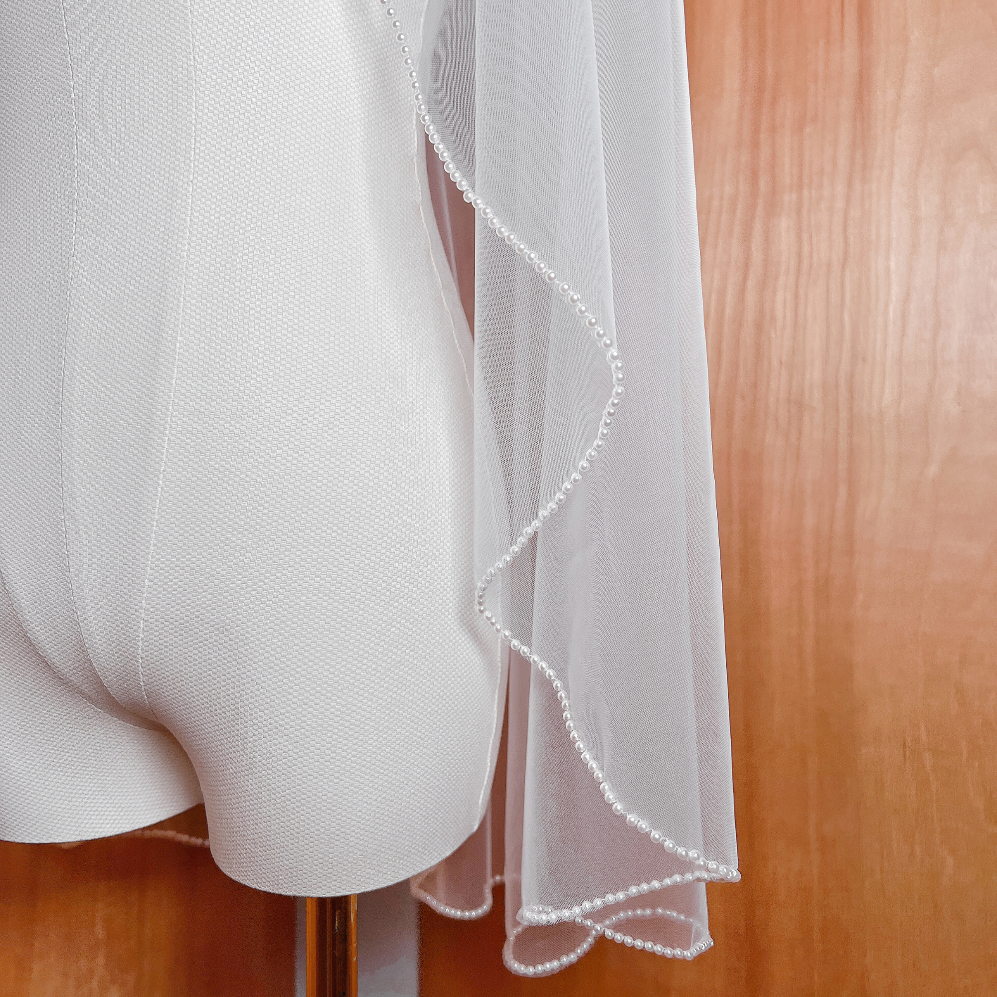 Close-up of a bridal veil featuring a dense cascading pearl trim along the edge, shown in ivory tulle at fingertip length.