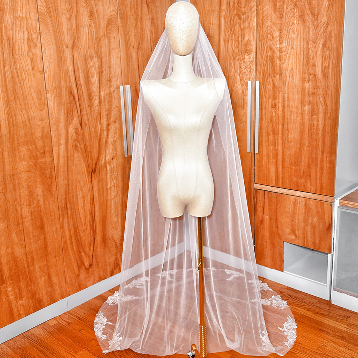 A long cathedral length floral applique wedding veil displayed on a mannequin.