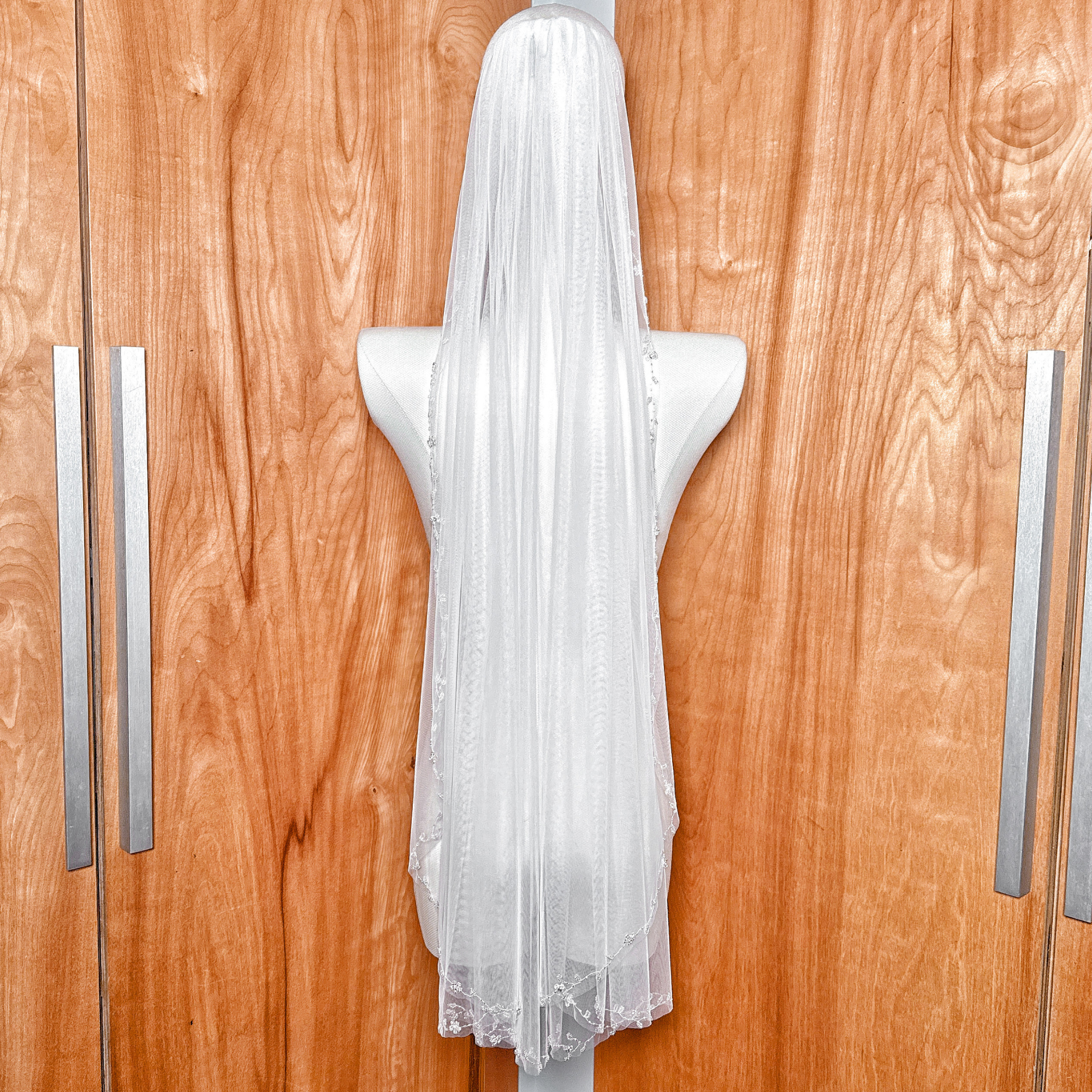 Back view of the sheer fingertip length floral beaded edge wedding veil cascading elegantly.