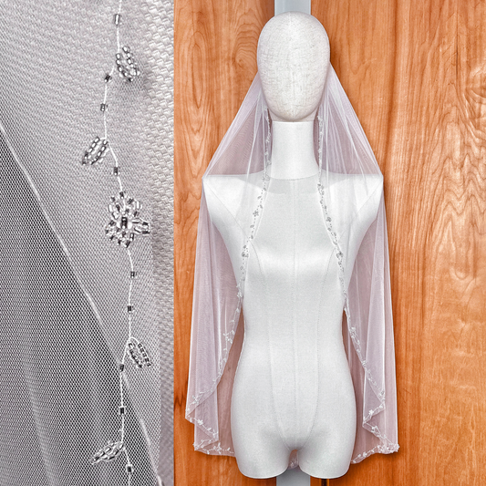 Fingertip length floral beaded edge wedding veil with intricate embroidery on a bridal display.