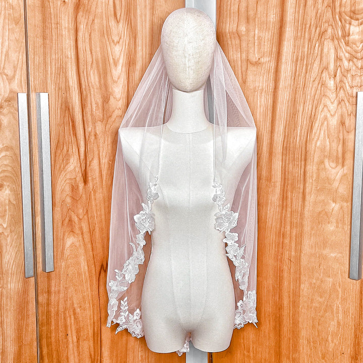 Fingertip length floral lace edge wedding veil displayed on a mannequin for a classic bridal look.