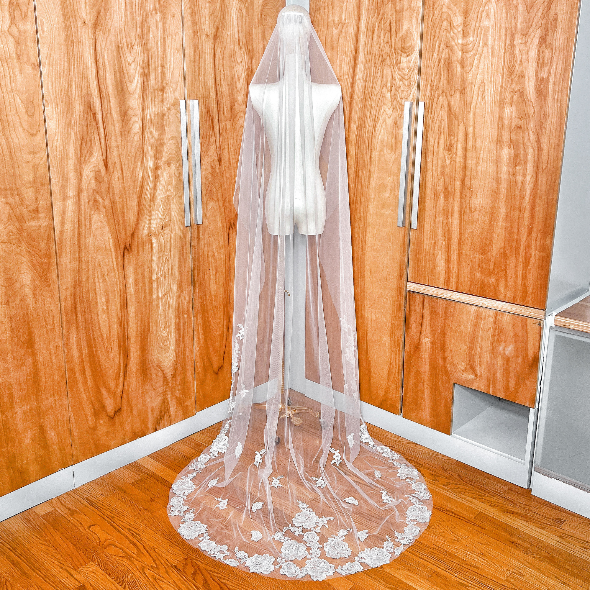 Back view of a floral lace edge wedding veil with long train on a bridal mannequin in chapel length.