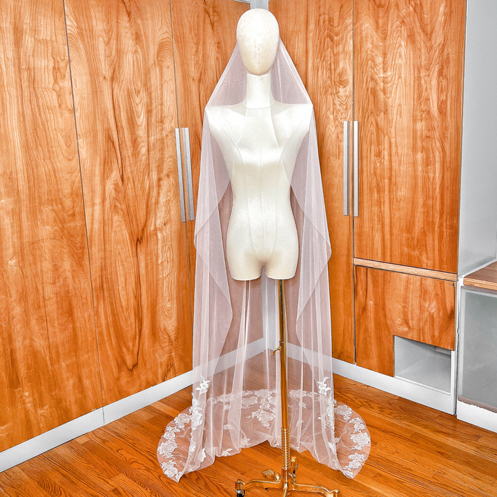 Chapel length floral lace edge wedding veil with long train draped over a mannequin.