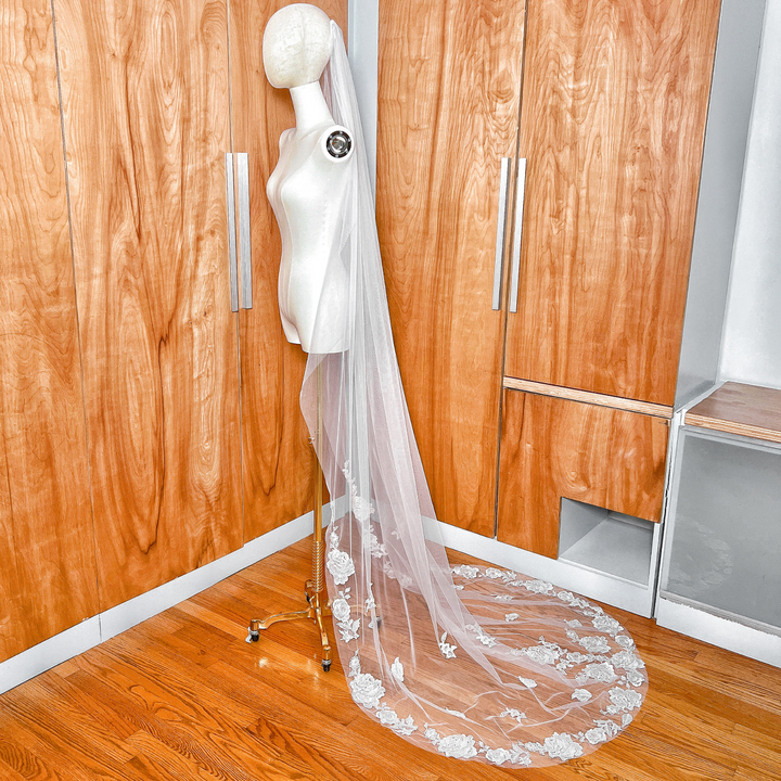 Side view of a chapel length floral lace edge wedding veil with long train on a dress form.