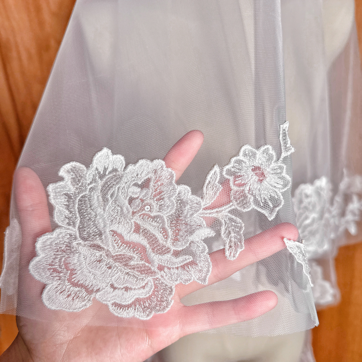 Detailed close-up of the floral lace embroidery on a two tier wedding veil at fingertip length.