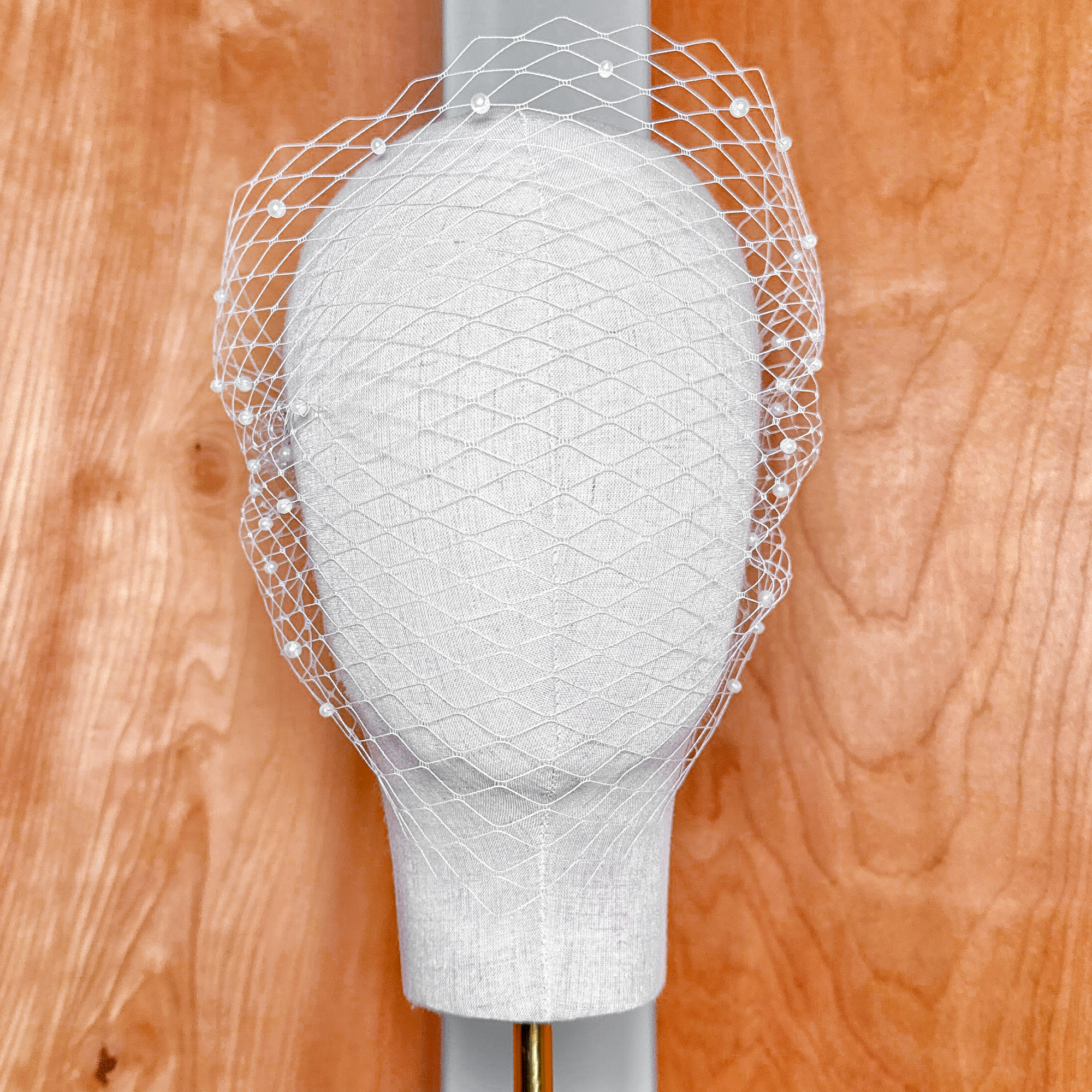 Front view of a classic net bandeau birdcage wedding veil with pearls attached to a bridal display head.