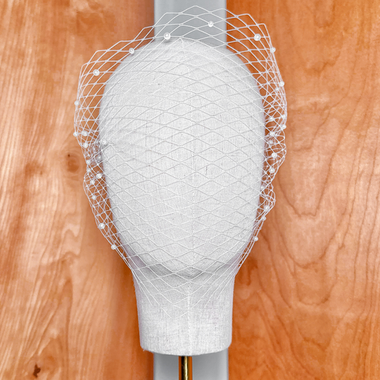 Front view of a classic net bandeau birdcage wedding veil with pearls attached to a bridal display head.