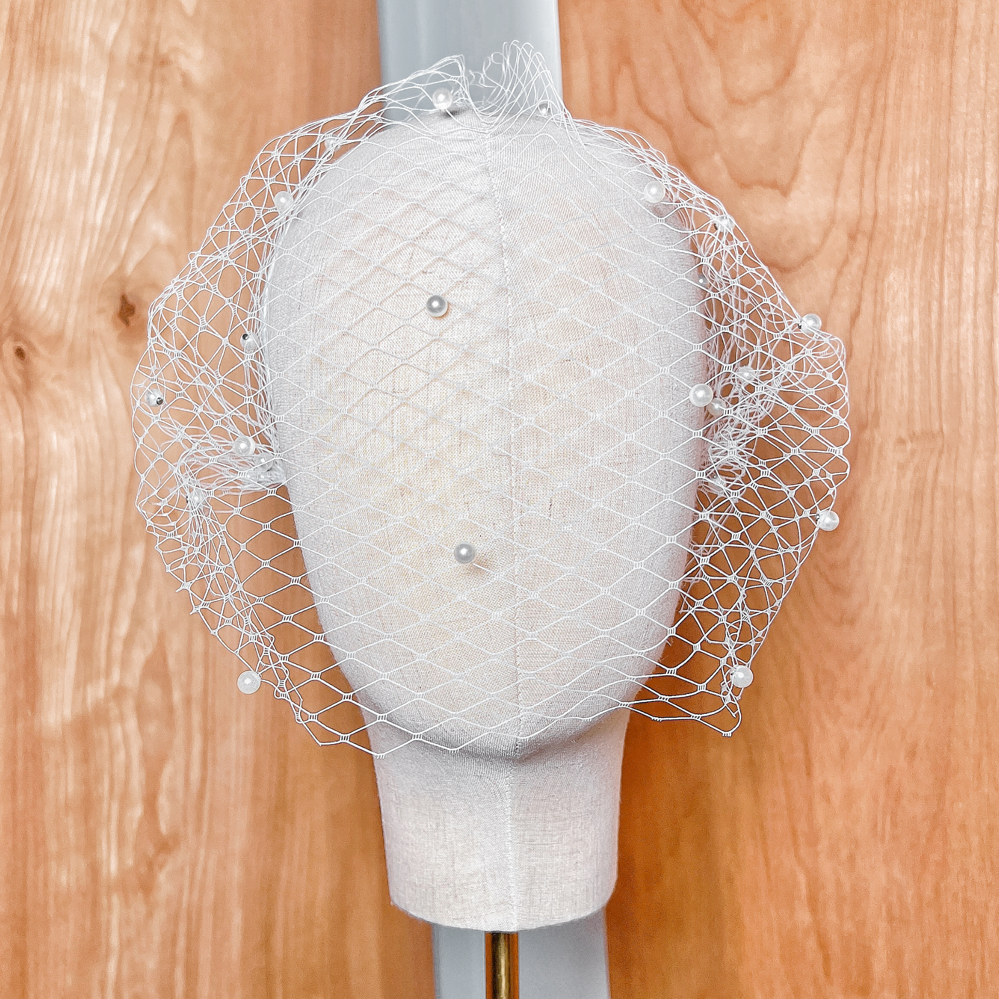 Front view of a bridal pearl birdcage wedding veil draped elegantly to showcase its shape and pearl embellishments.