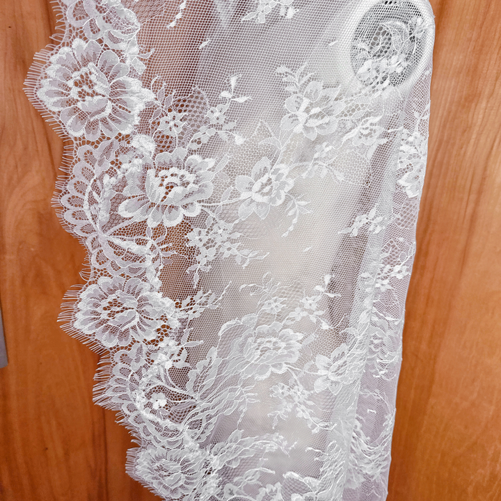 Close-up detail of the floral lace pattern on a waltz length mantilla veil, highlighting the delicate embroidery and scalloped edges.
