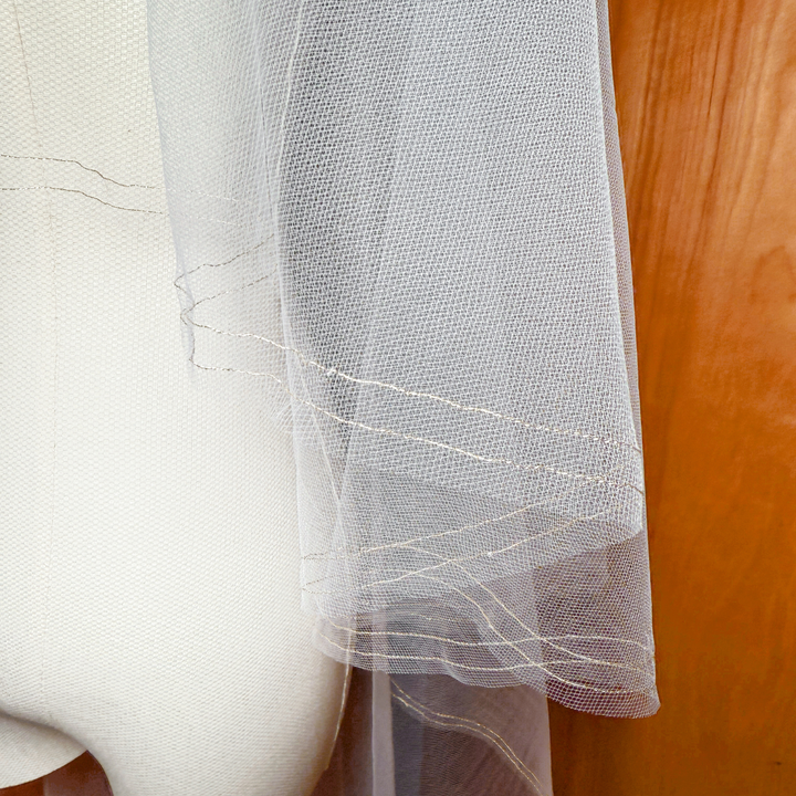 Close-up of a two tier veil featuring a gold metallic trim and blusher, displayed on a bridal mannequin in waltz length.