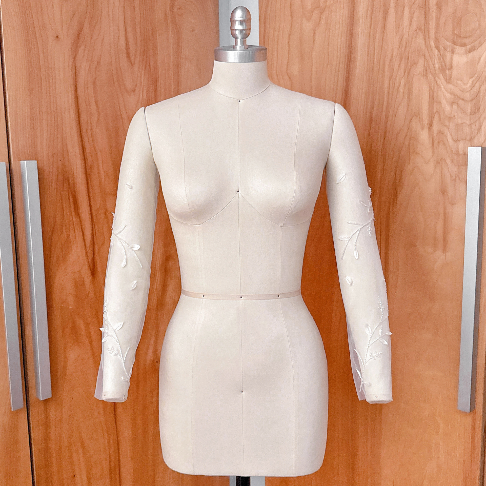 A side-angle studio shot of the beaded floral vine illusion sleeves on a dress form, showcasing the continuous botanical vine design down the length of the arm.