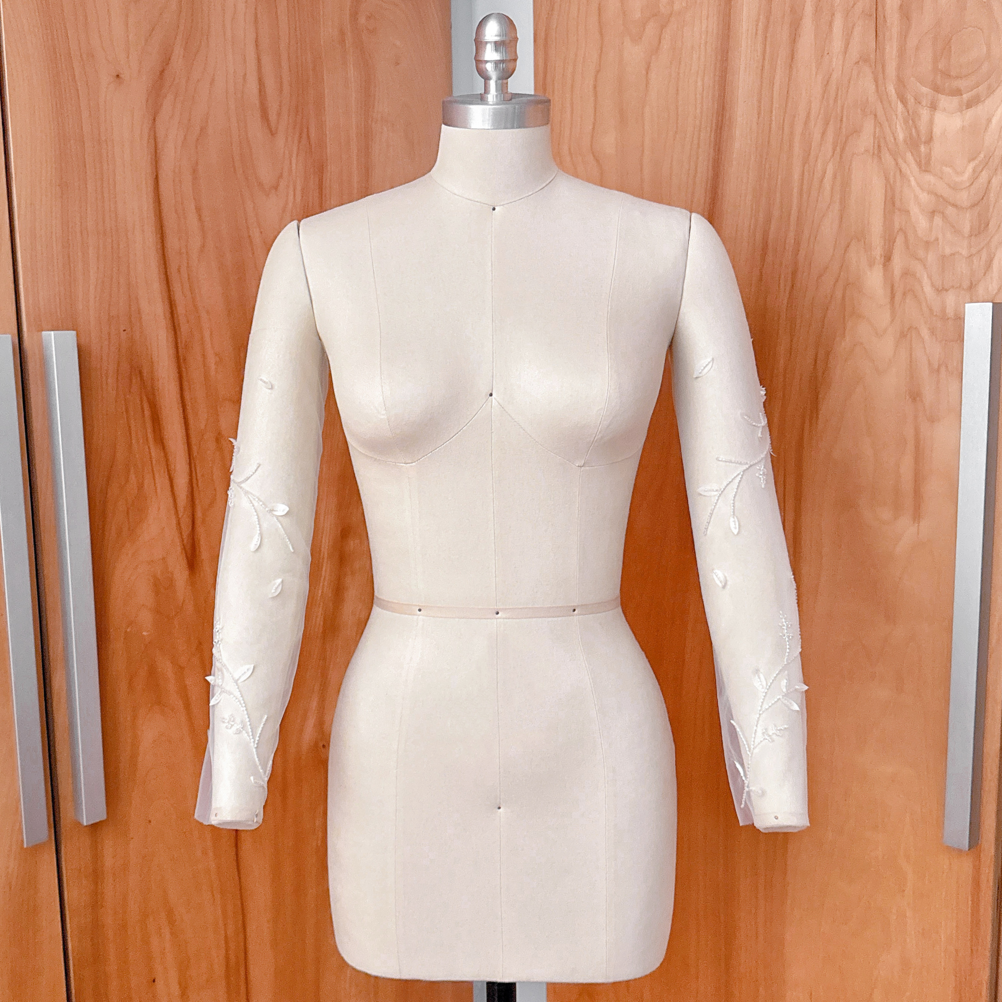 A side-angle studio shot of the beaded floral vine illusion sleeves on a dress form, showcasing the continuous botanical vine design down the length of the arm.