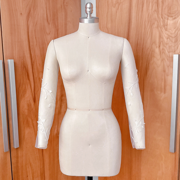 A side-angle studio shot of the beaded floral vine illusion sleeves on a dress form, showcasing the continuous botanical vine design down the length of the arm.