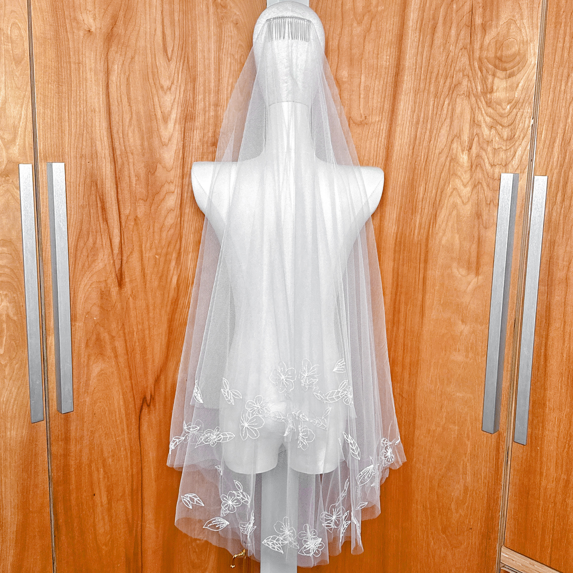 Back view of a fingertip length 3D floral embroidered veil cascading down a mannequin.