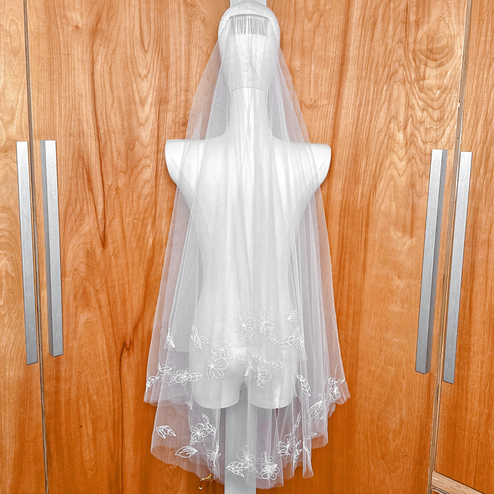 Back view of a fingertip length 3D floral embroidered veil cascading down a mannequin.