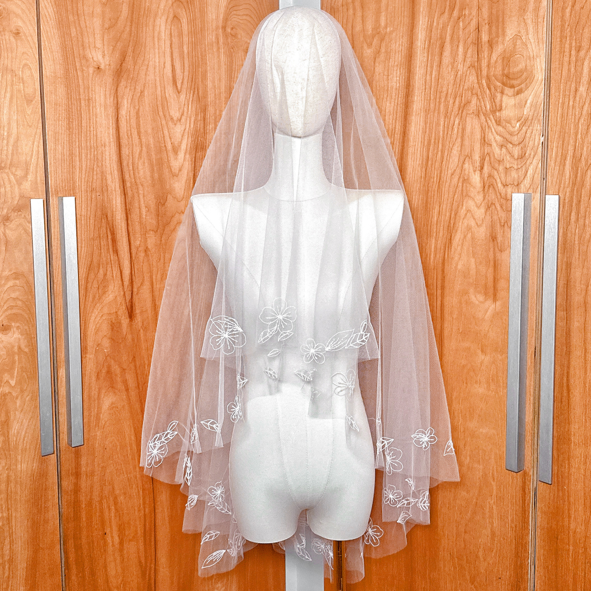 Fingertip length hand embroidered flower veil with white floral appliqués displayed on a mannequin.