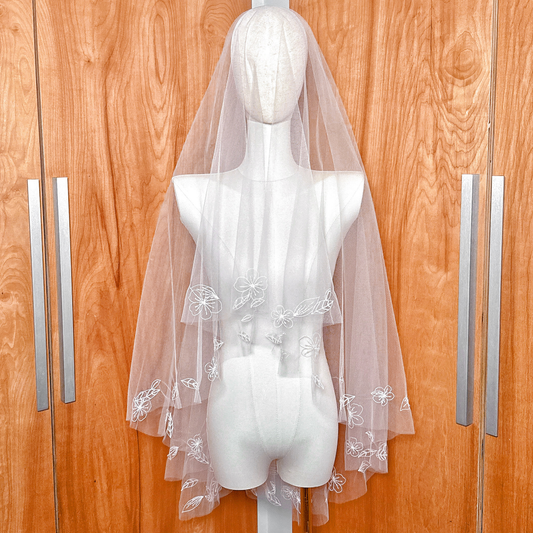 Fingertip length hand embroidered flower veil with white floral appliqués displayed on a mannequin.