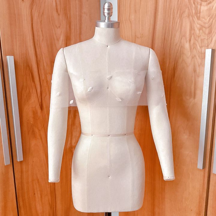 A side-angle studio shot of the 3D petal illusion bridal wrap on a dress form, showcasing the organic scatter and drape across the shoulders.