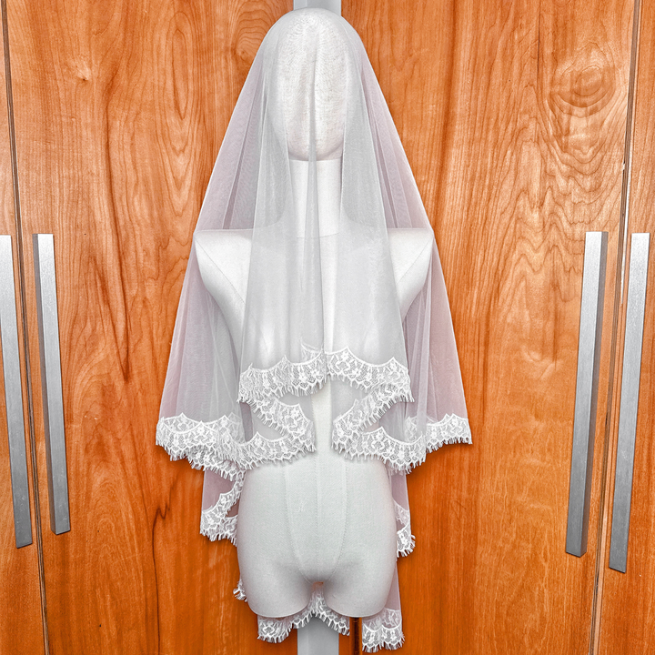 Front view of a hip-length lace trim drop wedding veil displayed on a mannequin, showcasing the intricate lace edge and sheer bridal tulle.