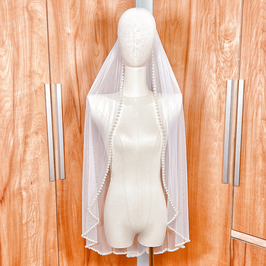Front view of a hip-length ivory wedding veil featuring a delicate pearl beaded edge.