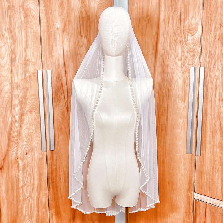 Front view of a hip-length ivory wedding veil featuring a delicate pearl beaded edge.