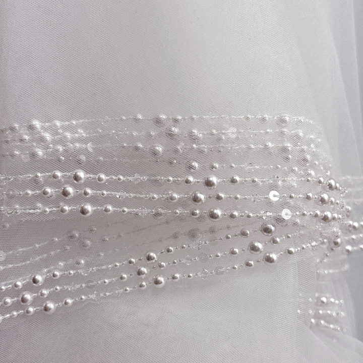 Close-up of intricate hand-beaded pearls and crystals on a white cathedral length wedding veil.