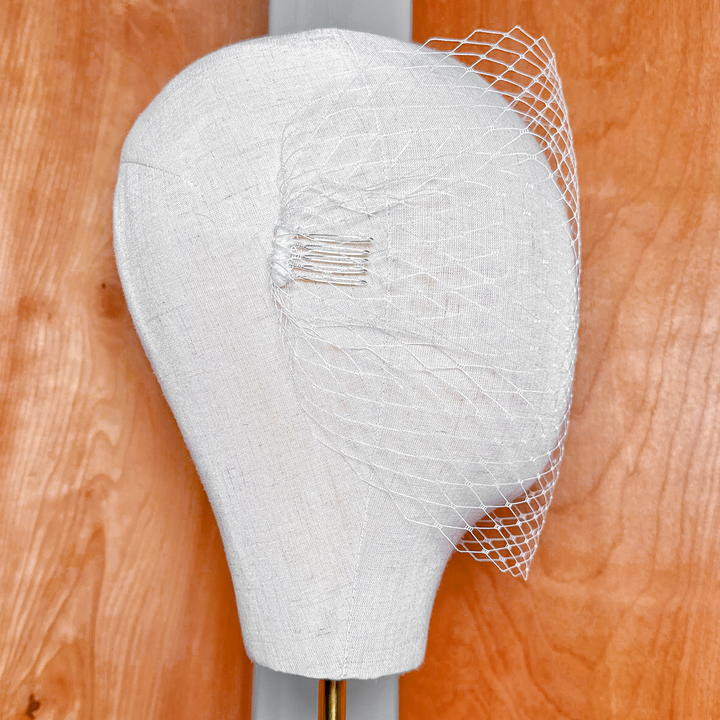 Detailed texture of an ivory bandeau birdcage wedding veil gathered on a display head.