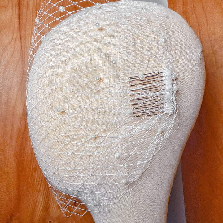 Detail shot of an ivory bandeau birdcage wedding veil with pearls on a display head.