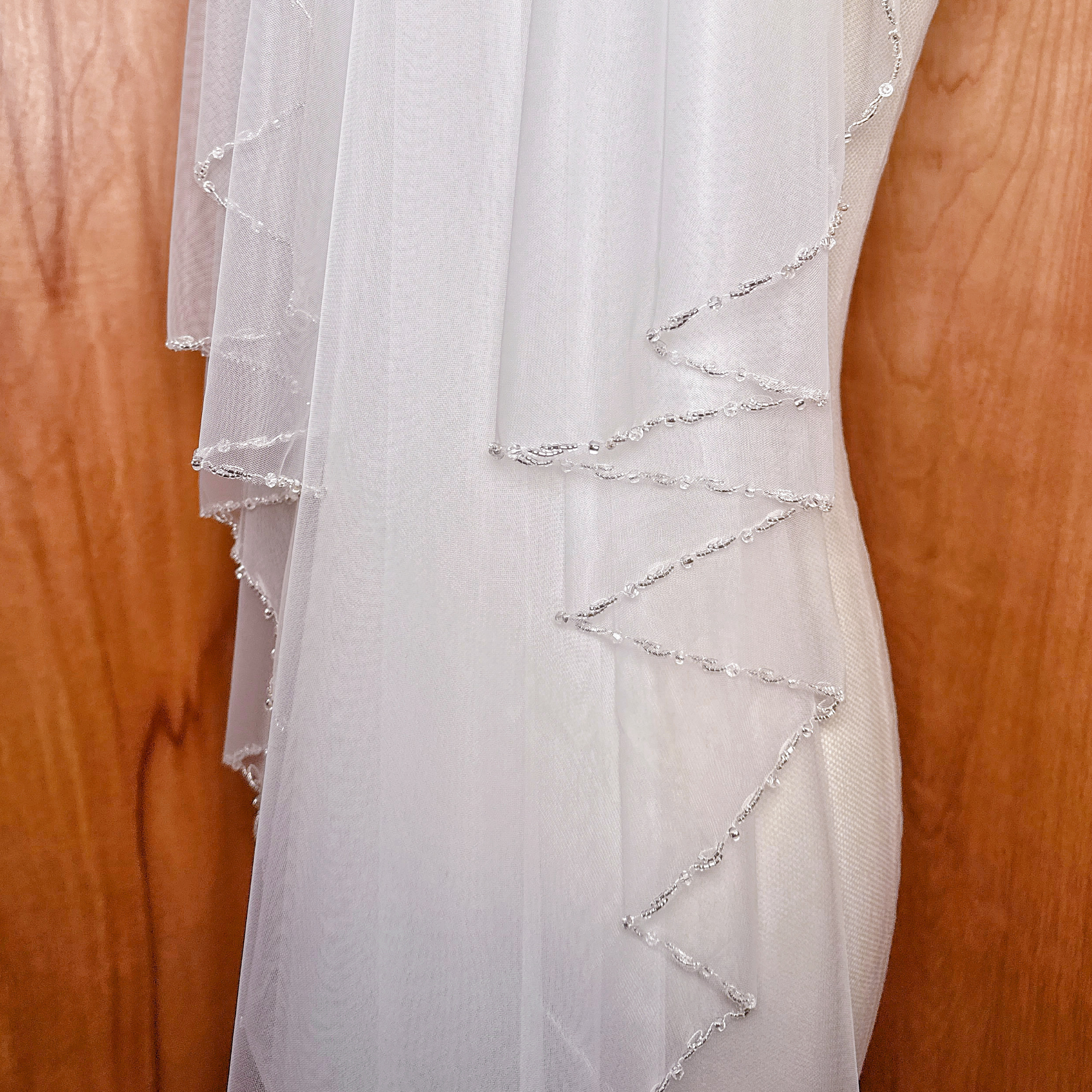 Waltz length ivory beaded edge wedding veil hanging gracefully.