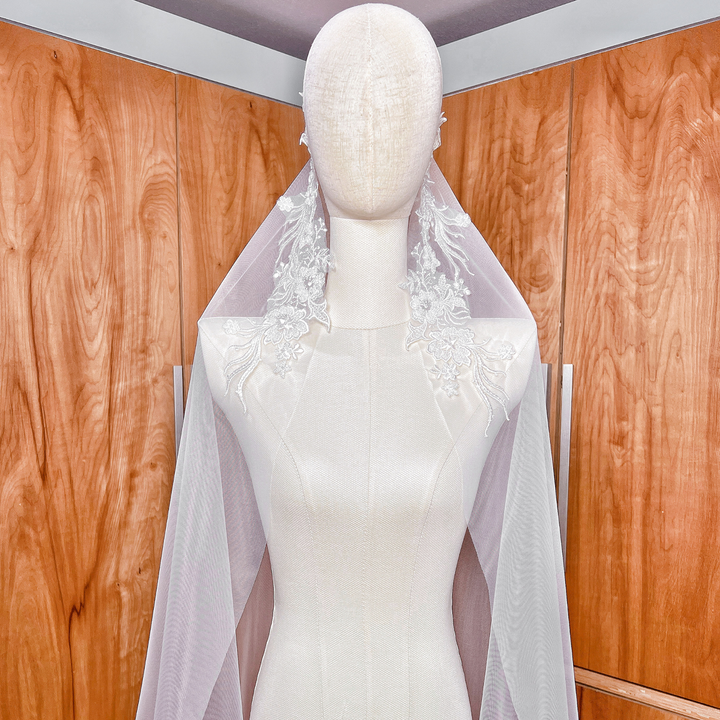 High-resolution detail of the ivory soft bridal tulle and beaded lace trim on a cathedral length mantilla veil displayed on a mannequin.