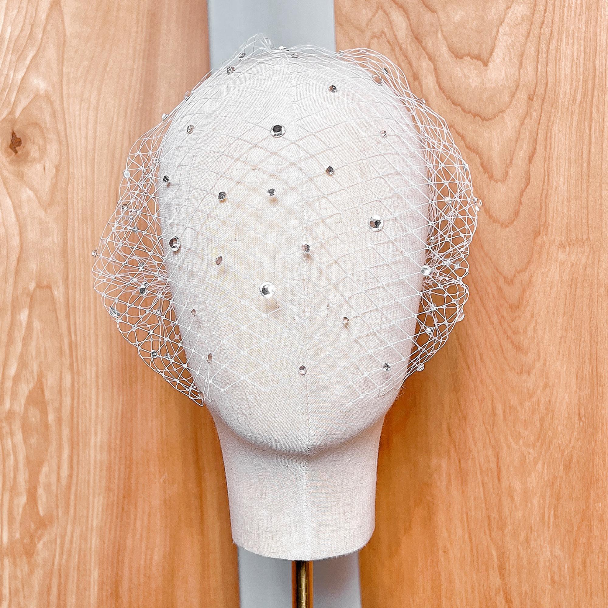 Detailed texture shot of an ivory crystal birdcage wedding veil draped over a studio display.