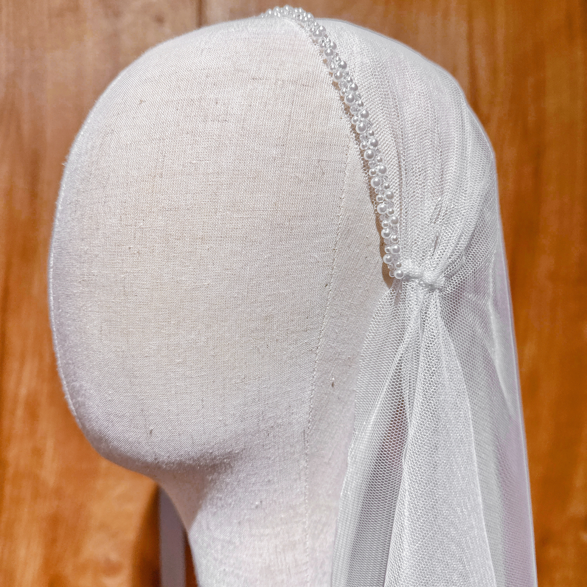 Ivory pearl-adorned beaded Juliet cap veil featuring a fingertip length silhouette on a bridal mannequin.