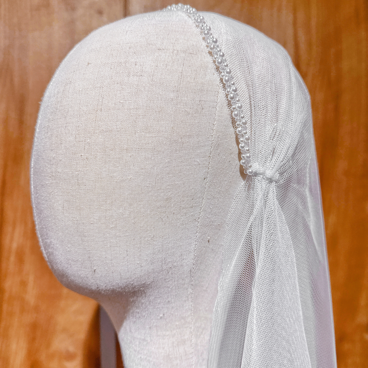 Ivory pearl-adorned beaded Juliet cap veil featuring a fingertip length silhouette on a bridal mannequin.
