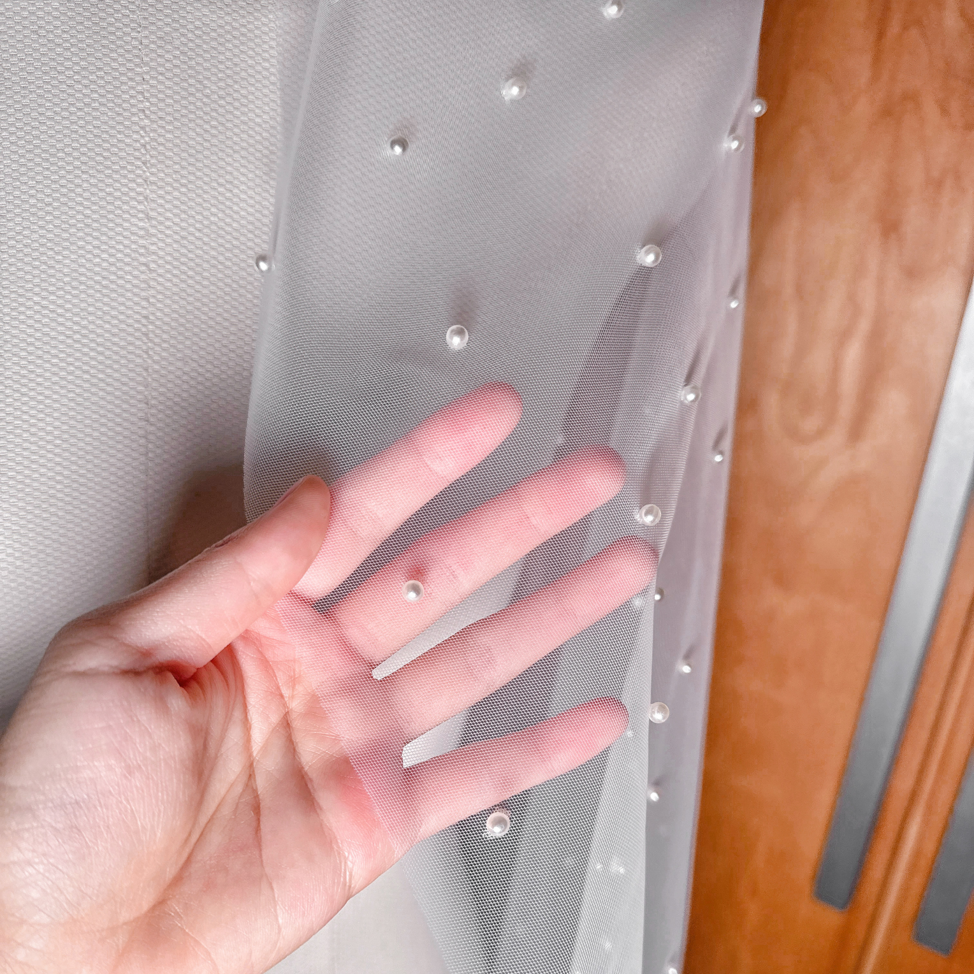 Close-up detail of hand-placed pearls on an ivory scattered pearl fingertip wedding veil with a sheer, elegant finish.