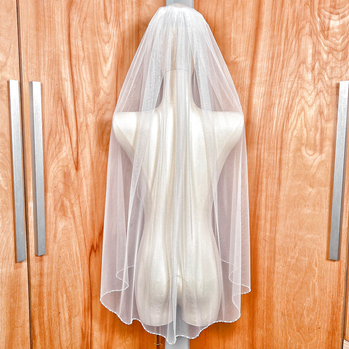 Back view of a fingertip length wedding veil with a pearl and crystal edge draping over soft ivory tulle.