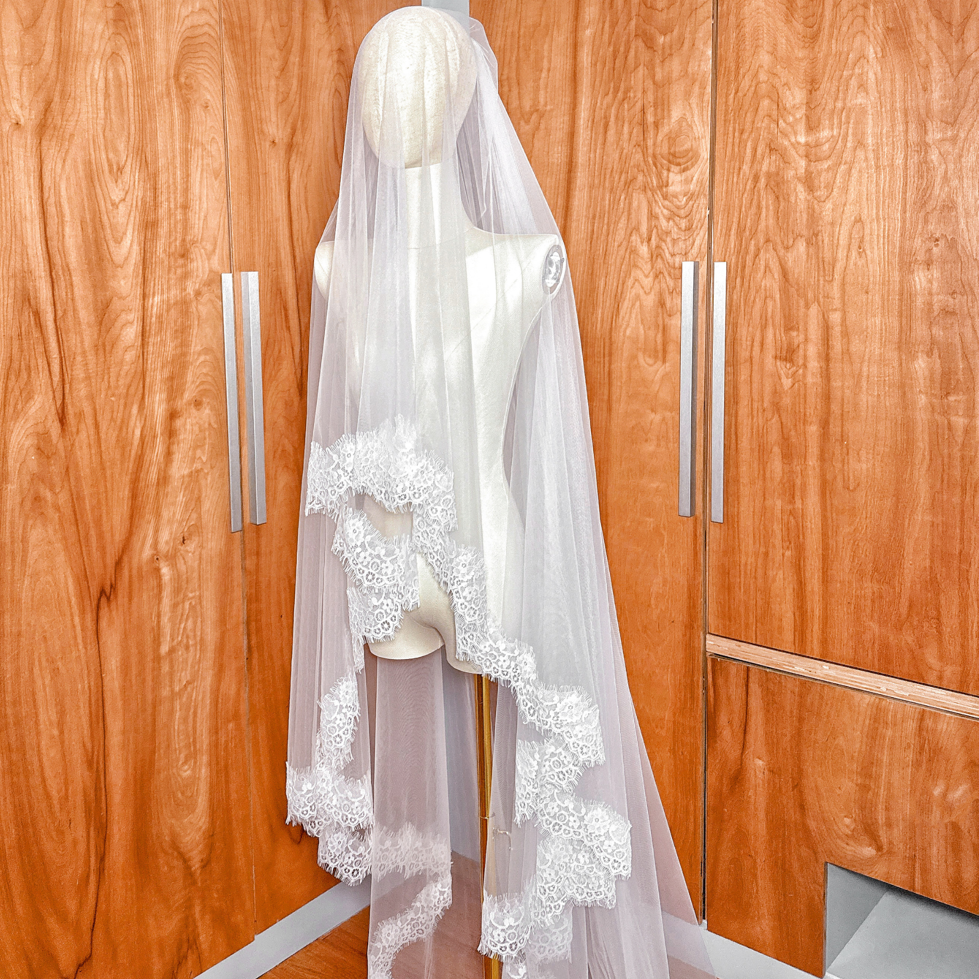 Ivory Two Tier Chantilly Lace Wedding Veil in cathedral length draped elegantly over a bridal mannequin.