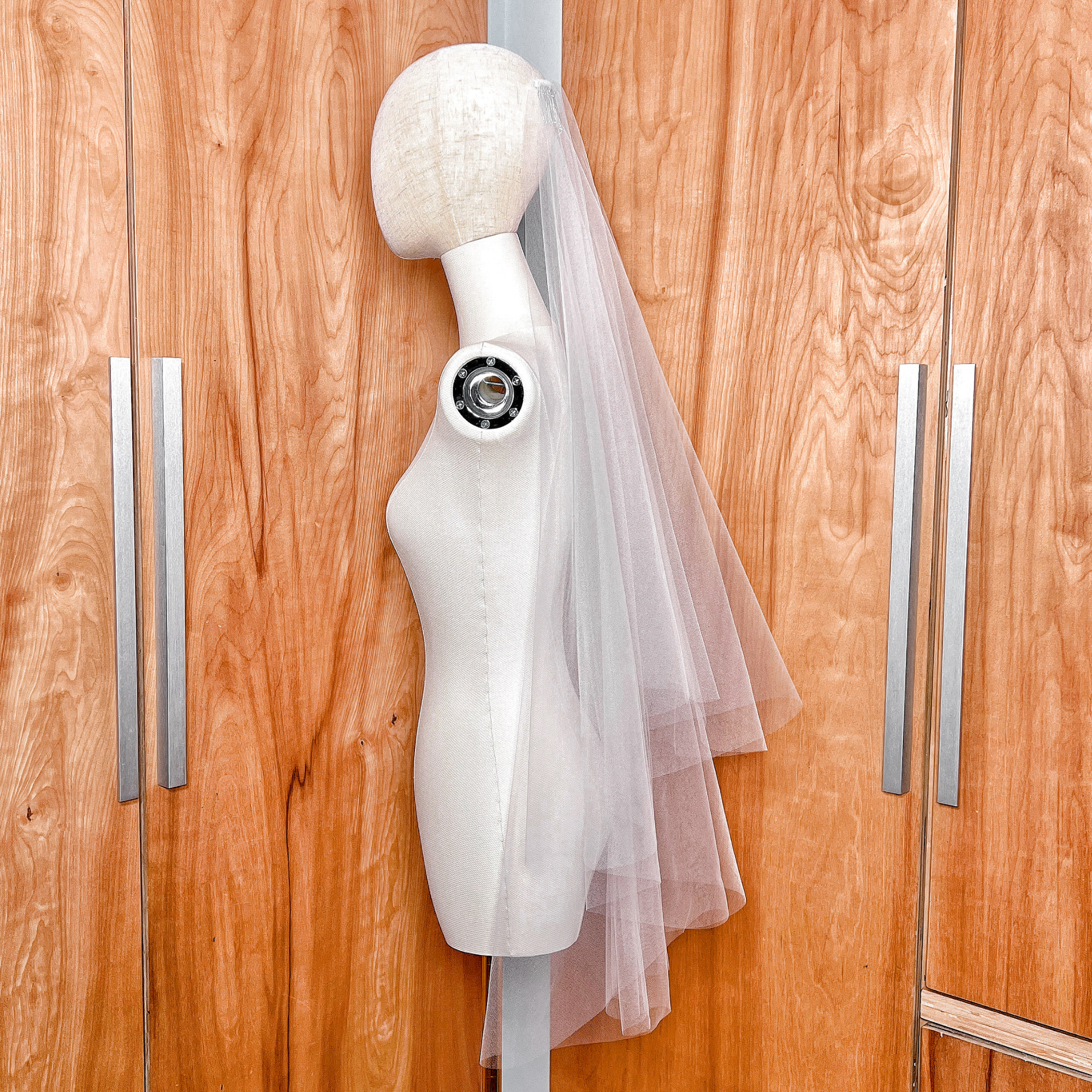 Side profile of a classic ivory two-tier fingertip length veil featuring a raw edge and front blusher.