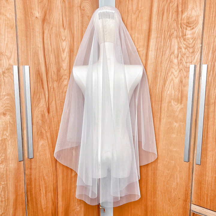 Back view of a double-layered fingertip length bridal veil featuring a classic raw cut edge in ivory tulle.