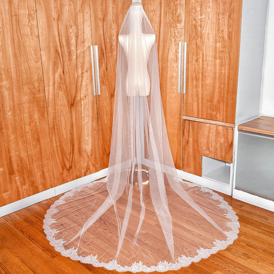 Back view of a long Chantilly lace cathedral wedding veil trailing behind a mannequin.