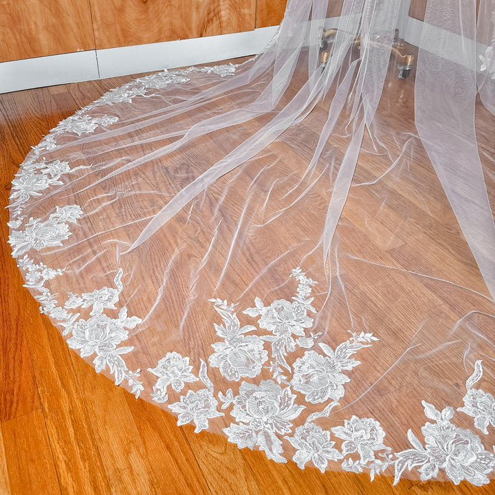 A delicate ivory lace edge wedding veil in a grand cathedral length displayed on a bridal mannequin.