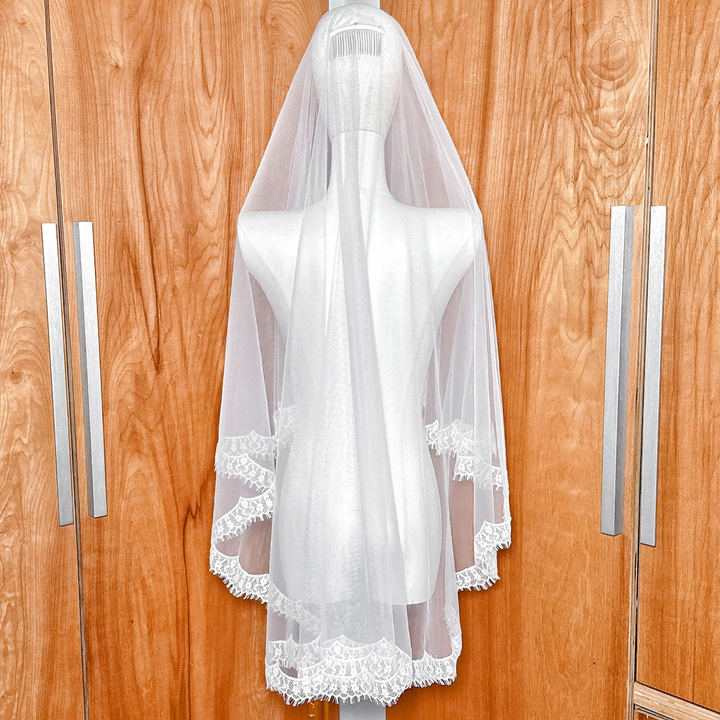 Back view of a bridal lace trim drop veil in hip length on a mannequin, highlighting the clean vertical fall and decorative lace border.