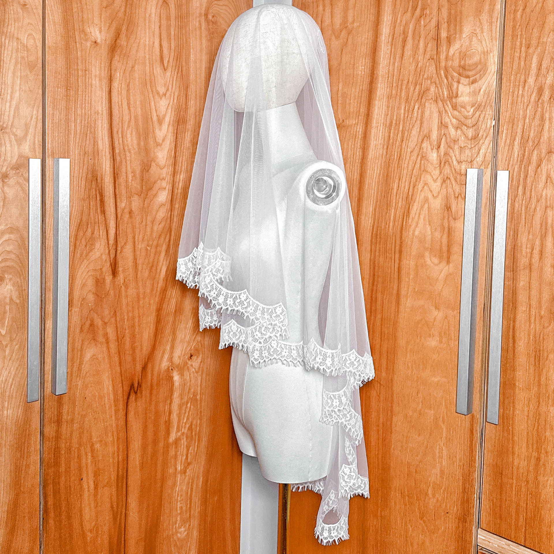 Side profile of a hip-length drop veil with lace edging on a mannequin, demonstrating the flat, no-gather comb attachment style.