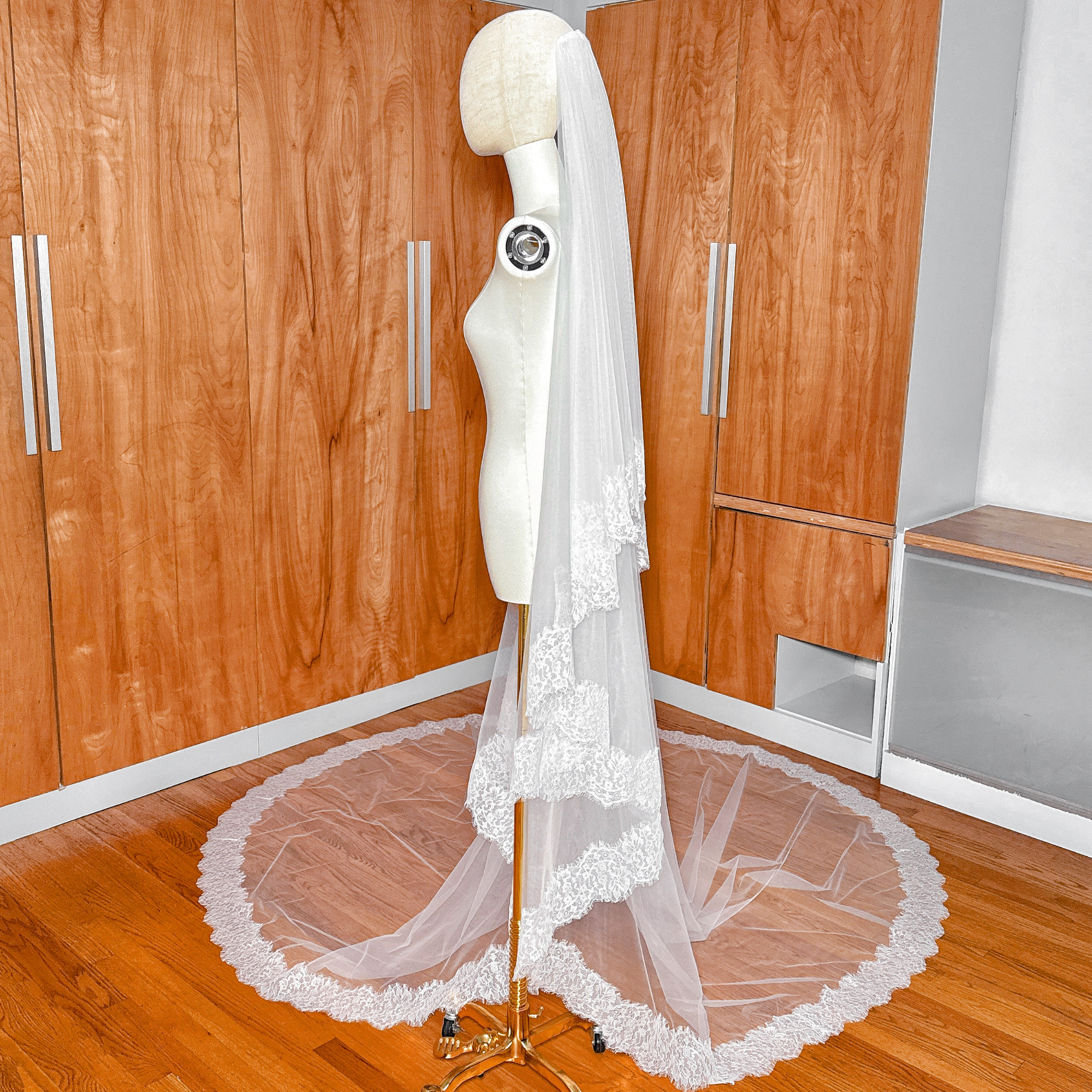 White Chantilly lace wedding veil draped over a dress form in a full cathedral length.