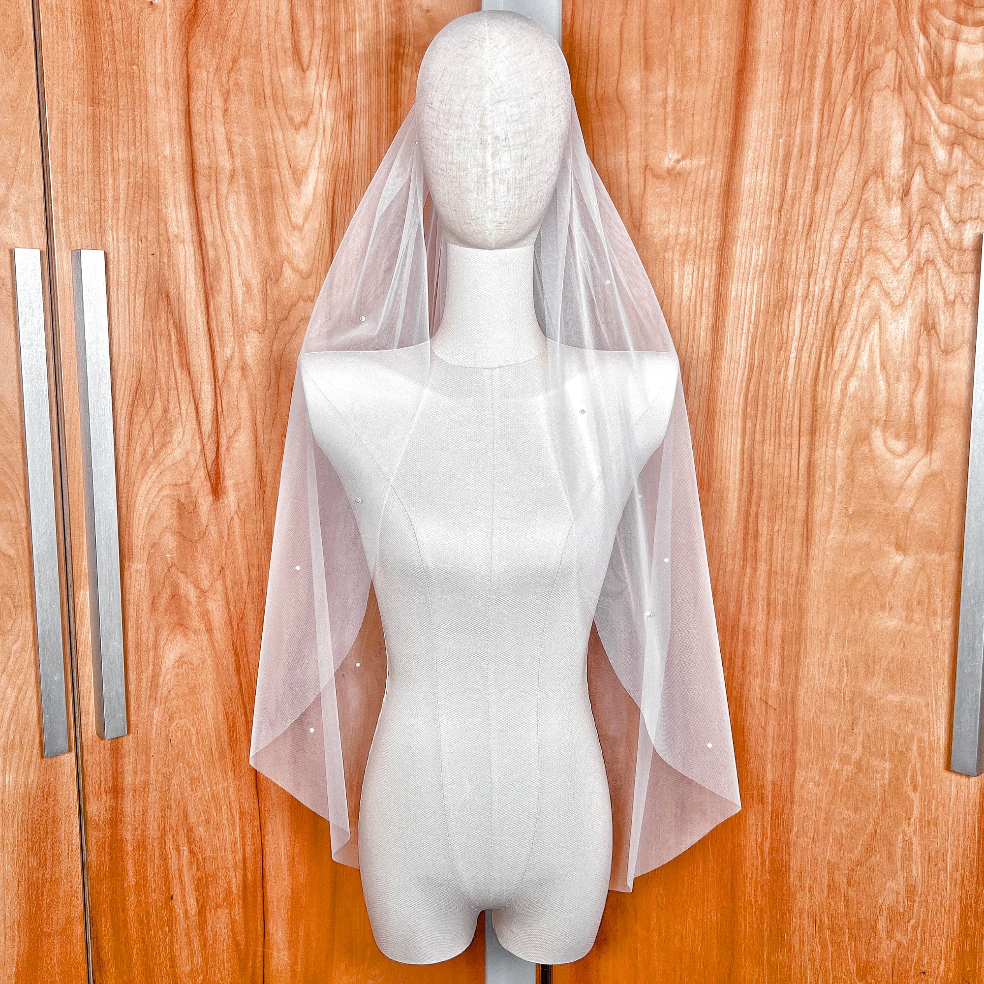 A fingertip length bridal veil with a light scattering of delicate pearls shown on a bridal display.