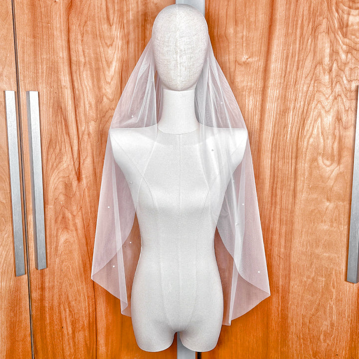 A fingertip length bridal veil with a light scattering of delicate pearls shown on a bridal display.