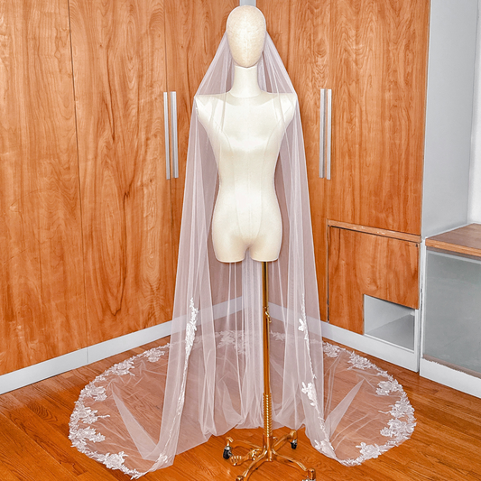 Full-length view of a traditional cathedral wedding veil featuring a wide lace border on a bridal mannequin.